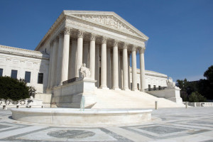 The front of the US Supreme Court in Washington, DC. Completed in 1935, the US Supreme Court building in Washington, DC, is the first to have been built specifically for the purpose, inspiring Chief Justice Charles Evans Hughes to remark, “The Republic endures and this is the symbol of its faith.” The Court was established in 1789 and initially met in New York City. When the national capital moved to Philadelphia, the Court moved with it, before moving to the permanent capital of Washington, DC, in 1800. Congress lent the Court space in the new Capitol building, and it was to change its meeting place several more times over the next century, even convening for a short period in a private house after the British set fire to the Capitol during the War of 1812. The classical Corinthian architectural style was chosen to harmonize with nearby congressional buildings, and the scale of the massive marble building reflects the significance and dignity of the judiciary as a co-equal, independent branch of government. The main entrance is on the west side, facing the Capitol. On either side of the main steps are figures sculpted by James Earle Fraser. On the left is the female Contemplation of Justice. On the right is the male Guardian or Authority of Law. On the architrave above the pediment is the motto “Equal Justice under Law.” Capping the entrance is a group representing Liberty Enthroned, guarded by Order and Authority, sculpted by Robert Aitken. At the east entrance are marble figures sculpted by Hermon A. MacNeil. They represent great law givers Moses, Confucius, and Solon, flanked by Means of Enforcing the Law, Tempering Justice with Mercy, Settlement of Disputes between States, and Maritime and other functions of the Supreme Court. The architrave carries the motto “Justice the Guardian of Liberty.” The interior of the building is equally filled with symbolic ornamentation. The main corridor is known as the Great Hall and contains double rows of mar