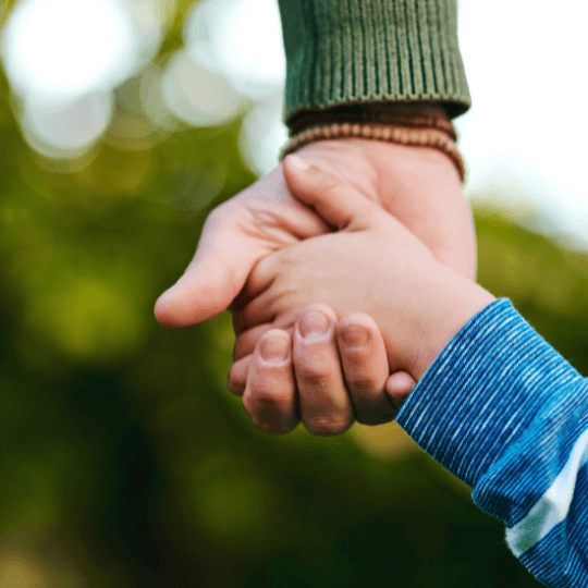 Close-up of an adult holding a child’s hand, representing trust and care for special needs individuals.